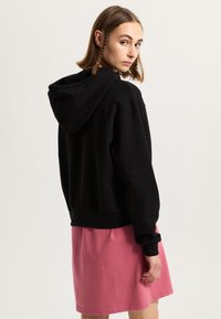 Svart croppad hoodie i mjukt tyg, med huva och ribbad mudd, kombinerad med en rosa knälång kjol.
