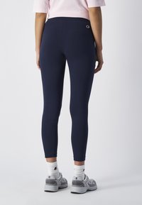 Granatowe legginsy wykonane z elastycznego materiału, z bezszwowym pasem w talii i małym logo na plecach. Dopasowany krój o długości do kostek.