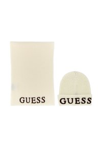 Gorro de punto blanco y bufanda a juego que presenta "GUESS" en letras marrones en el puño y en el borde inferior, respectivamente. Tejido texturizado.