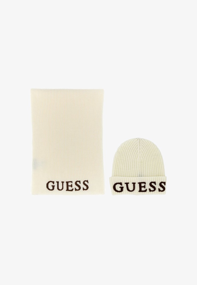 Gorro de punto blanco y bufanda a juego que presenta "GUESS" en letras marrones en el puño y en el borde inferior, respectivamente. Tejido texturizado.