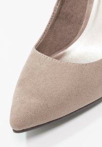 Beżowy zamszowy but na wysokim obcasie z ostrym noskiem i gładką, wewnętrzną wyściółką, prezentujący minimalistyczny design i subtelne detale szwów.