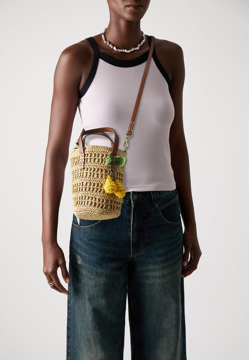 Woven straw bucket bag with green and yellow crochet fruit accents, leather handles, and an adjustable shoulder strap.