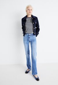 Chaqueta de mezcla de lana de color marino con botones de latón, camisa a rayas con el texto "PARÍS", jeans de color azul claro y mocasines de charol negros con detalles de perlas.