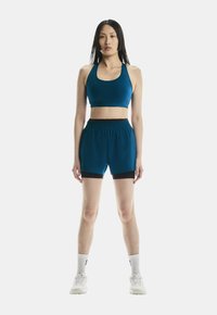 Atletiekset in teal, bestaande uit een cropped sportbh en bijpassende shorts met zwarte accenten. Glad textuur, slim fit ontwerp, met een elastische tailleband.