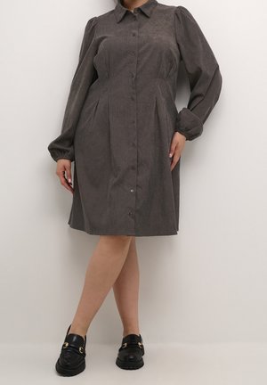 Szara sukienka z długimi bufkami, zapinana na guziki z przodu, z plisowanym wzorem. W połączeniu z czarnymi mokasynami ozdobionymi złotymi detalami.
