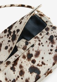 Brown and cream spotted crossbody bag with a smooth texture, featuring a flap closure and black satin lining inside.