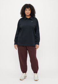 Čierne polo tričko s dlhým rukávom, golierom a logom Nike, v kombinácii s vínovými teplákmi a svetlými športovými topánkami.