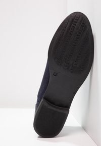 Scarpa in suede blu navy con suola in gomma testurizzata, caratterizzata da una silhouette liscia e un design minimalista. Gli accenti includono un tallone pulito e battistrada.