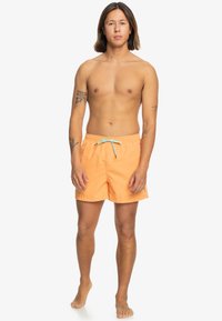 Oranje zwembroek met een elastische tailleband en een verstelbaar turkoois trekkoord. Heeft een gladde textuur en een klein logo detail.