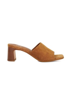 Mules à talons ouverts en daim marron avec un talon carré. Présentent une texture lisse, une large bride supérieure et une semelle intérieure profilée pour le confort.