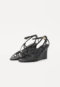 Sandales noires à talon compensé avec plusieurs brides entrecroisées, un design noué à l'avant et une bride à la cheville. Texture lisse et design minimaliste.