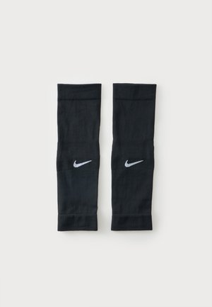 Ζευγάρι μαύρα συμπιεστικά μανίκια Nike με λευκά λογότυπα Swoosh, τοποθετημένα επίπεδα σε απλό φωτεινό φόντο.