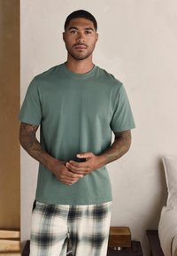T-shirt en coton vert à manches courtes et col rond. Associé à un pantalon de pyjama à carreaux dans des tons crème, noir et gris.