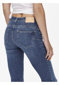 Skinny jeans i mörkblå denim med hög midja, två bakfickor och en tanfärgad etikett vid midjan. Slät yta.