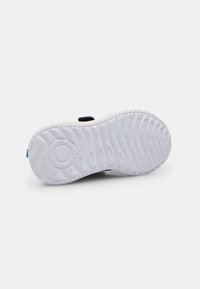 Vit gummisula med texturerat greppmönster, cirkulär mönsterdetalj och delvis vy av en fäst svart rem ovanför.