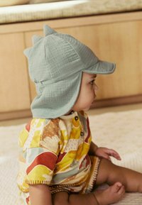 Hele sinine puuvillane müts kolme tõstetud tipuga ja laia äärisega. Värvikas mustriga jumpsuit, kus on kujutatud loomi ja abstraktseid kujundeid.