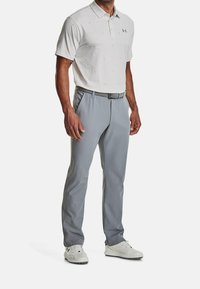 Miesten golfvaatteet, joissa on vaaleanharmaa kuviollinen polo-paita ja harmaat golfhousut. Asusteena valkoiset golfkengät ja musta vyö.