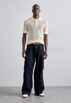 Polo a maniche corte beige in maglia con tre bottoni e dettagli ricamati, abbinato a pantaloni cargo blu scuro dal taglio morbido con tasche.