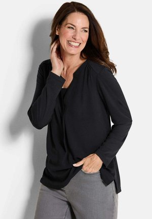 Black long-sleeve top with a V-neckline, soft texture, and side slits, paired with gray pants. Simple design, no visible patterns or hardware.