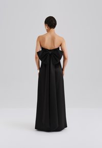 Vestido negro sin tirantes con un gran lazo en la parte posterior, con una tela suave y fluida que crea una silueta elegante. Detalles texturizados realzan el diseño.