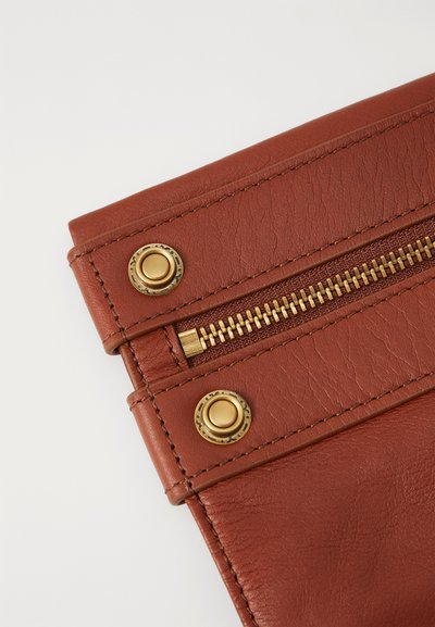 Brown leather bag corner with a gold zipper, featuring brass snap buttons and visible stitching. Smooth texture and structured design.