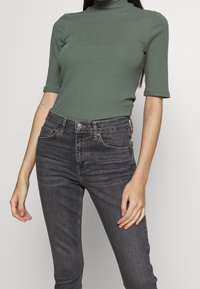 Zelený žebrovaný rolák s krátkými rukávy, spárovaný s tmavě šedými slim-fit džíny s klasickými kapsami a knoflíkovým zapínáním.