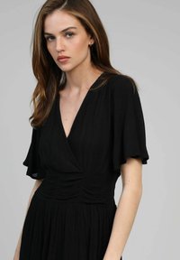 Robe noire avec des manches courtes et flottantes et un décolleté en V. Dotée d'un tissu texturé et d'une taille froncée pour une silhouette fluide.