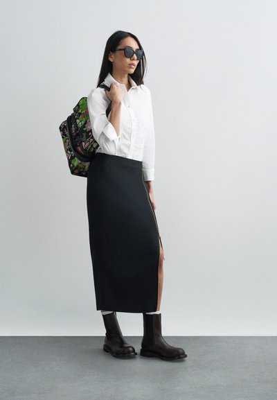 Μαύρη midi φούστα με πλαϊνό φερμουάρ, λευκό πουκάμισο με κουμπιά, σκούρα γυαλιά ηλίου και σακίδιο με floral σχέδιο· χοντρά καφέ μποτάκια αστραγάλου.