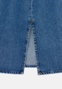 Denimska krila s srednje modro barvo, zasnovo z odprtinami spredaj, raztrganim robom in kontrastnim rumenim šivom ob šivih.