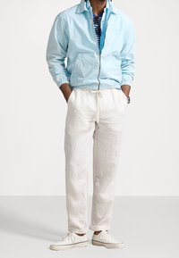 Ljusblå lättviktsjacka, randig skjorta under, vita linnbyxor och vita sneakers. Avslappnad passform med elastiska muddar.