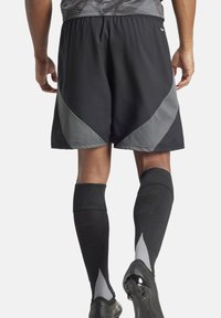 Schwarze Sportshorts mit grauen Akzenten, aus leichtem Material; kombiniert mit schwarzen kniehohen Socken und Fußballschuhen.
