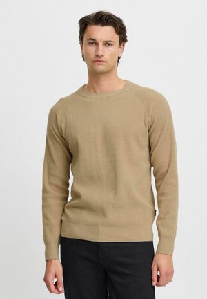Beige knit sweater with a round neckline and raglan sleeves. Textured material, fitted style, paired with dark jeans. Simple design.