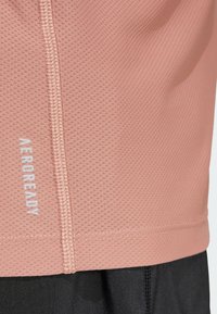 Maglietta AeroReady traspirante di colore rosa pallido, caratterizzata da un motivo a rete testurizzato, cuciture a contrasto e un logo discreto vicino all'orlo.
