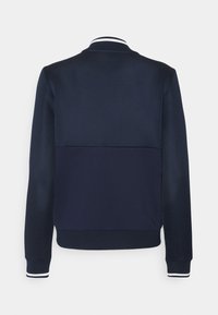 Mörkblå jacka med en texturerad nätövre, solid nederdel, ribbade muddar och en vitrandig krage.