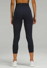 Svarta high-waisted leggings i stretchmaterial, figursydd design, cropped längd, med en liten logotyp nära vänster vad.
