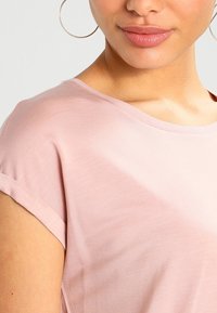 T-shirt di cotone rosa chiaro con maniche arrotolate e scollatura a barca, caratterizzato da una texture liscia e un tessuto morbido che cade bene.