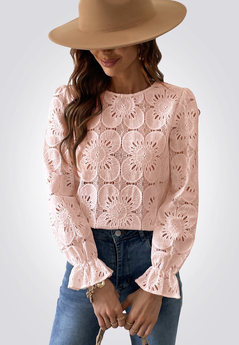 Roze kanten top met bloemenpatronen, lange mouwen, gerimpelde manchetten en een ronde halslijn, gecombineerd met blauwe jeans en een beige hoed.