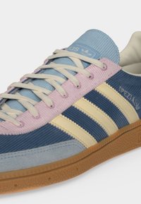 Κοντινή λήψη ενός μπλε και ροζ παπουτσιού Adidas με κρεμ ρίγες και λευκά κορδόνια σε σόλα από καουτσούκ.