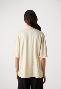 Camicia a maniche corte, con colletto, in tessuto beige chiaro. Vestibilità comoda con una texture liscia e orlo arrotondato. Dettagli di cucitura sottili.