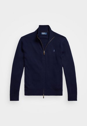 Marineblå zip-genser laget av myk strikket stoff. Har høy krage, to frontlommer og en liten brodert logo på brystet.