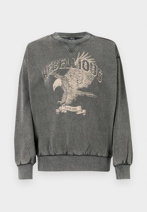 Grå sweatshirt med en lös passform, som har en rund halsringning och elastiska ärmslut. Tryckt design av en örn med ordet "REBELLIOUS" och "sedan 1995."
