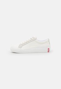 Baskets en toile blanches avec une semelle en caoutchouc, un bout rond et un logo rouge à l'arrière. Présentent un système de fermeture à lacets et des panneaux latéraux texturés.