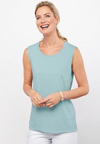 Canotta azzurro chiaro senza maniche con scollo rotondo, realizzata in tessuto morbido. Senza fantasie, abbinata a pantaloni bianchi, indossata con un bracciale leggero.