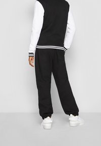 Giacca sportiva bianca e nera con polsini a righe e pantaloni della tuta neri. Le sneakers bianche completano l'outfit, caratterizzate da un design elegante.