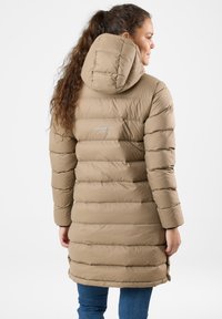 Beżowy pikowany płaszcz z kapturem, z poziomymi przeszyciami, błyszczącym wykończeniem i logo z tyłu. Nosi się go z niebieskimi dżinsami.