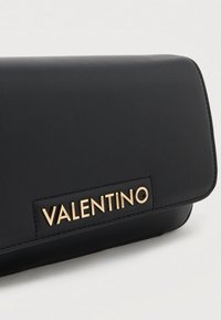 Czarna skórzana kopertówka z magnetycznym zapięciem na klapę, z teksturowaną powierzchnią i złotym logo „VALENTINO” na froncie.