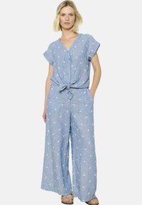 Mono azul de chambray con mangas cortas, botón frontal, cintura con lazo, perneras anchas y un patrón blanco de hojas en toda la prenda. Incluye dos bolsillos laterales.