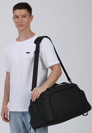 Sac de voyage noir en matériau durable, doté d'une bandoulière, de poignées supérieures et de plusieurs compartiments zippés pour le rangement.