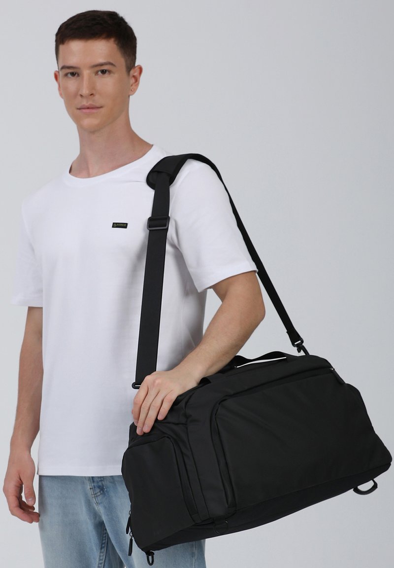 Borsa da viaggio nera realizzata in materiale resistente, dotata di una tracolla, maniglie superiori e più scomparti con zip per la conservazione.