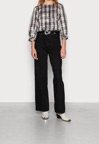 Mustat korkeavyötäröiset housut yhdistettynä ruudulliseen, pitkähihaiseen puseroon, jossa on rento istuvuus ja puffihihat. Täydennetty nilkkasaappailla.